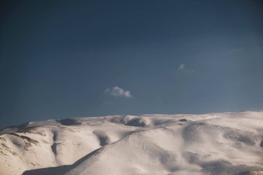 Karlı, mavi gökyüzü ve bulutlu bir dağın manzarası..