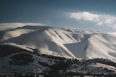 Karlı, mavi gökyüzü ve bulutlu bir dağın manzarası..