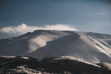 Karlı, mavi gökyüzü ve bulutlu bir dağın manzarası..