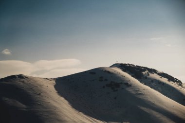Karlı, mavi gökyüzü ve bulutlu bir dağın manzarası..