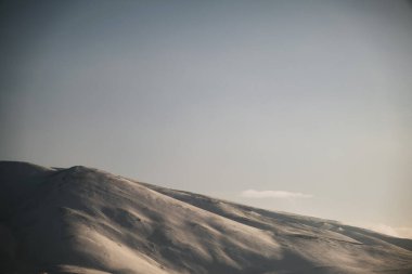 Karlı, mavi gökyüzü ve bulutlu bir dağın manzarası..