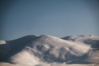 Karlı, mavi gökyüzü ve bulutlu bir dağın manzarası..