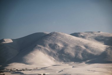 Karlı, mavi gökyüzü ve bulutlu bir dağın manzarası..