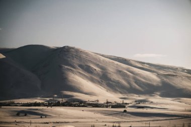 Kar ve köy manzaralı bir dağ, mavi gökyüzü ve biraz bulut..
