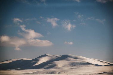 Karlı, mavi gökyüzü ve bulutlu bir dağın manzarası..