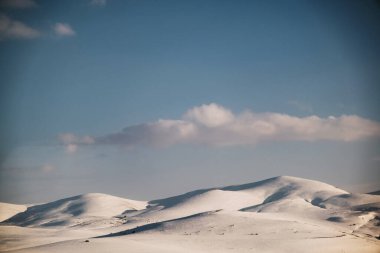 Karlı, mavi gökyüzü ve bulutlu bir dağın manzarası..