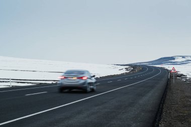 Kış mevsiminde hareketli, bulanık şeritli ve karlı asfalt ve bükülmüş bir yolun çapraz görüntüsü..
