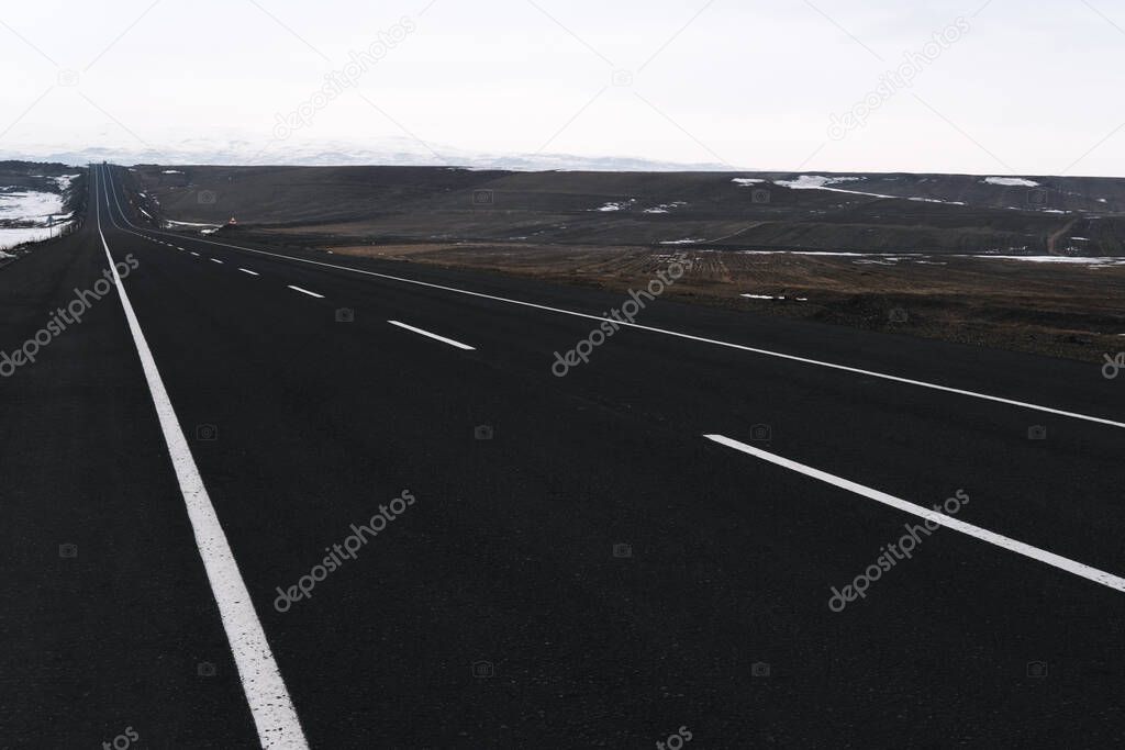 Diagonal view of an emtpy asphalt and bending road with lanes and snow in winter.