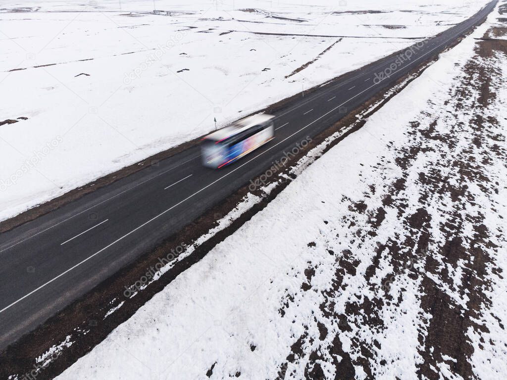 Aerial diagonal view of a road with one lane and snow in winter with a bus and motion blur