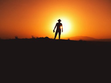 Tepede gün batımında fötr şapkalı bir adamın silueti.