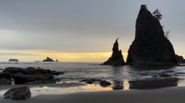 Sunset over the Pacific Ocean behind the rock stack silhouette at Rialto Beach with the water gently lapping at the shore. Olympic National Park, La Push - Washington.