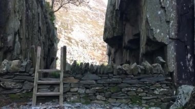 A plus-sized woman climbs a ladder stile over a dry stone wall leading into a narrow gorge on a hiking trail in Snowdonia National Park. Llyn Idwal, North Wales, UK