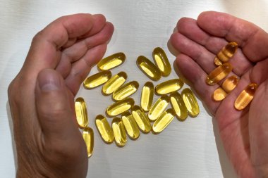 Vitamin kapsülleri avuçlarda, beyaz masada yakın plan.