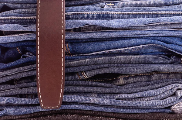 Leather belt close-up on stack of denim trousers stock of various models and colors — Zdjęcie stockowe