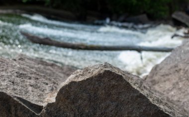 Dağlık nehrin fırtınalı akışının bulanık arka planında yakın plan gri granit taşı