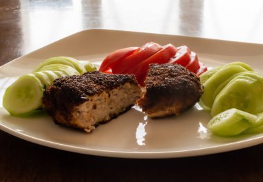 Appetizing freshly cooked cutlet close-up with tomato and cucumber slices on white plate on the table