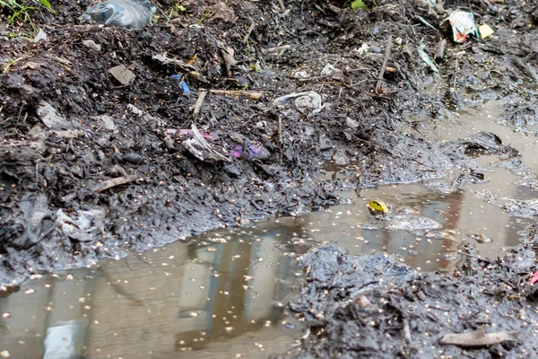 Liquid mud of urban garbage with blurry reflection of windows of house in dirty puddle of water