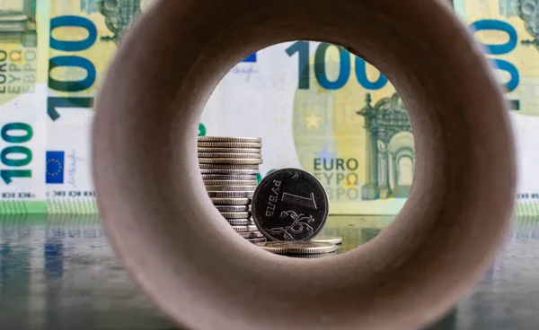 1 russian ruble coin close-up on background of euro banknotes inside blurred paper pipe background