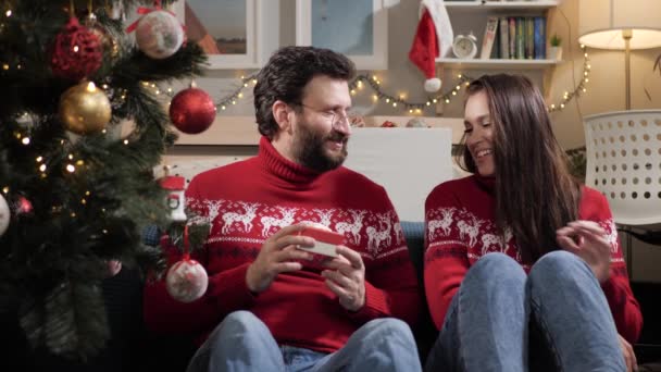 Dando presentes de Natal. Casal feliz homem e mulher sentam-se no chão perto da árvore de Natal e dar presentes uns aos outros. Movimento lento — Vídeo de Stock