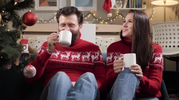Christmas, new year, eve. Happy couple man and woman sit on floor and look at Christmas tree, drink tea and talk. Slow motion — Stock Video