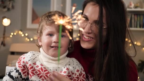 Vánoční světla, jiskry. Šťastná usměvavá žena a dítě 2-3 let pohled na jiskru, vánoční věnce v pozadí. Detailní záběr a zpomalení — Stock video