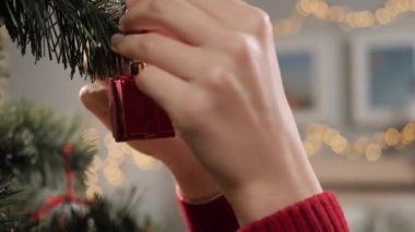 Noel ağacı süsleme, dalda oyuncak. Kırmızı kazaklı kadın elleri Noel ağacının dalına Noel oyuncakları koyuyor ve parmağıyla itiyor. Yakın çekim ve yavaş çekim
