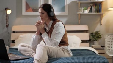 Kadın görüntülü konuşuyor. Kulaklıklı bir kadın akşamları yatak odasında yatağında oturur ve bilgisayardan biriyle konuşur. Yavaş çekim görünümü