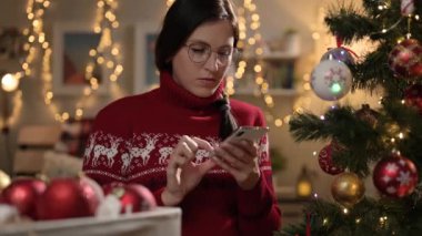 Noel arifesinde çalışan bir kadın. Düşünceli kadın yılbaşı ağacını süslüyor ve akıllı telefondan mesaj yazarak dikkati dağılıyor.