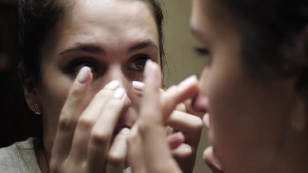 Woman squeezes out black dots on her nose. Woman looks in mirror and with her fingers presses on skin of her nose to squeeze out black dots. Close-up — Stock Video