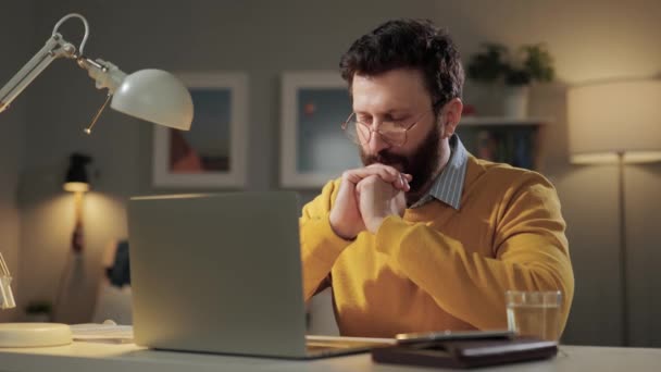 El hombre está rezando. Hombre barbudo trastornado con gafas en casa oficina se sienta en el escritorio con el ordenador portátil y dice la oración — Vídeos de Stock