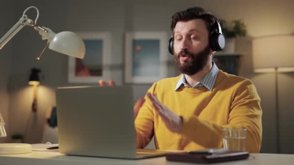 男は停止、感情を示していません。コンピュータのウェブカメラを見て自宅のオフィスでヘッドフォンを持つ深刻な不満髭の男と彼の手のひらを示しています停止 — ストック動画