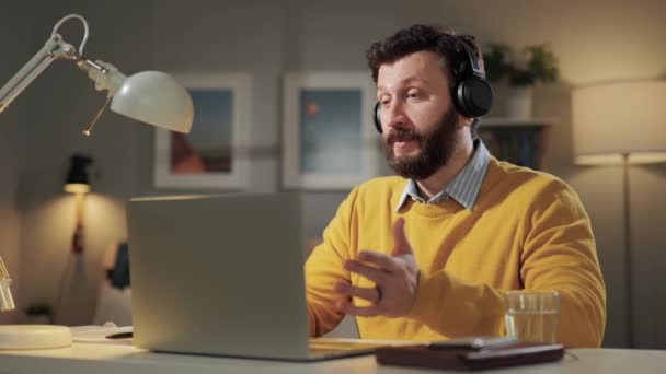 Man shows OK. Positive smiling bearded man with headphones in home office looking at computer webcam and shows OK gesture with his fingers — Stock Video