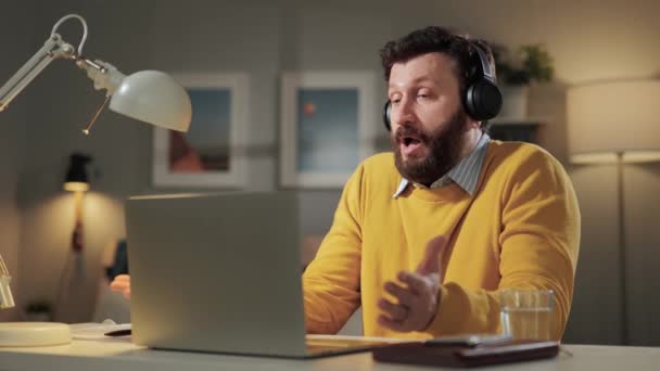 シュラグわからない。家のオフィスでヘッドフォンを持つ複雑な髭の男は、コンピュータのウェブカメラを見て、感情的に彼の肩を絞る — ストック動画