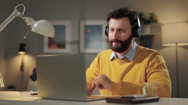 Поважайте лук, вітаючі емоції. Бородатий чоловік з навушниками в домашньому офісі дивиться на комп'ютерну веб-камеру і кладе руку на груди і луки — стокове відео
