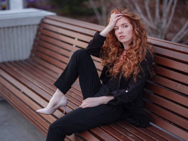 Kızıl genç kadın bahar şehrinde yürüyor. İş kadını bankta oturuyor.