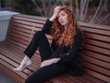 Kızıl genç kadın bahar şehrinde yürüyor. İş kadını bankta oturuyor.