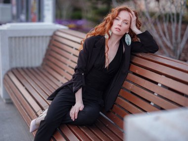 Kızıl genç kadın bahar şehrinde yürüyor. İş kadını bankta oturuyor.