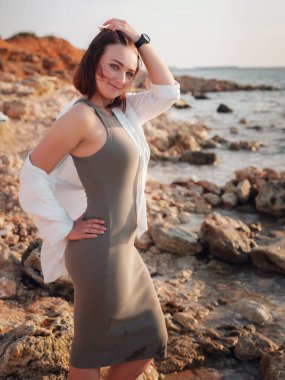 çekici sakin genç bayan denizin kenarında duruyor ve sevinçlerini ifade ediyor. Güneşin son ışıklarının tadını çıkararak gün batımına karşı poz veriyor..