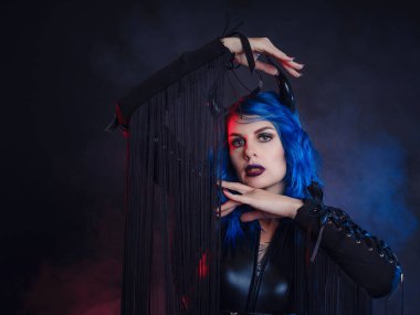 Şeytan. Cadılar Bayramı partisinde siyah boynuzlu ve lateks elbiseli komik bir şeytan. Şeytan kostümü. duman kırmızı ve mavi, yeraltı atmosferi.