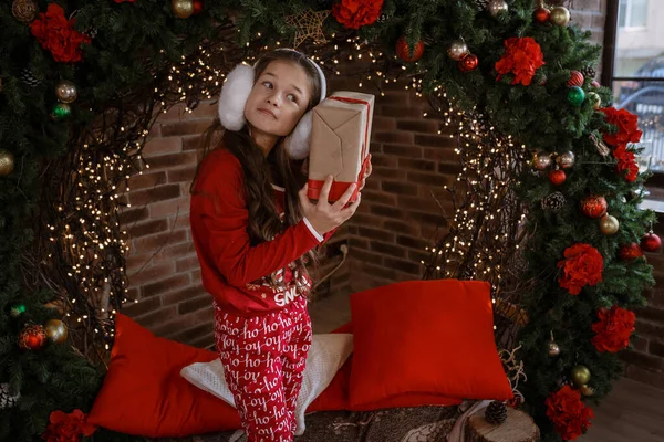 パジャマの黒い髪の女の子とギフトボックスを保持します ロフトスタイルのインテリア背景にクリスマスの装飾 — ストック写真