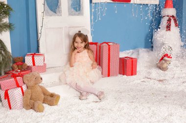 Noel ağacının altında gülümseyen, süslemeli bir kız çocuğu. Yeni yıl. Kış tatili.