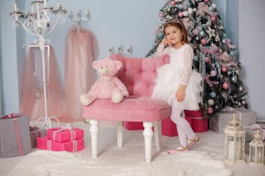 Noel ağacının altında gülümseyen, süslemeli bir kız çocuğu. Yeni yıl. Kış tatili.