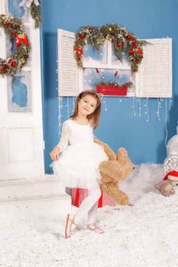 Noel ağacının altında gülümseyen, süslemeli bir kız çocuğu. Yeni yıl. Kış tatili.