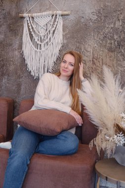 Beyaz el yapımı makromlu sarışın kadın. Odanın duvarında, içi rahat bir şekilde duruyor. Boho tarzı yatak odasında doğal malzemeli yeni pamuk örgü. Ev dekorasyonu kavramı