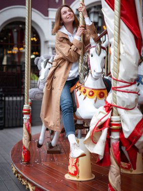 Güzel bej ceketli kadın sonbahar bulutlu Moskova 'da yürüyor, atlıkarıncanın keyfini çıkarıyor ve eğleniyor. Sokak tarzı. Rusya 'ya Seyahat.