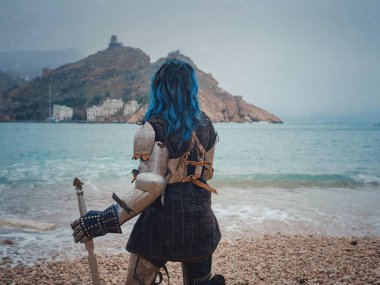 Ortaçağ şövalyesi kadın savaş öncesi dua ediyor. Orta Çağ tarihi fantezi fotoğrafı. Güzel bayan şövalye sahilde, dağların yakınında denizin üzerindeki karı seyrediyor.