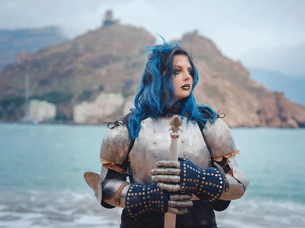 Ortaçağ şövalyesi kadın savaş öncesi dua ediyor. Orta Çağ tarihi fantezi fotoğrafı. Güzel bayan şövalye sahilde, dağların yakınında denizin üzerindeki karı seyrediyor.