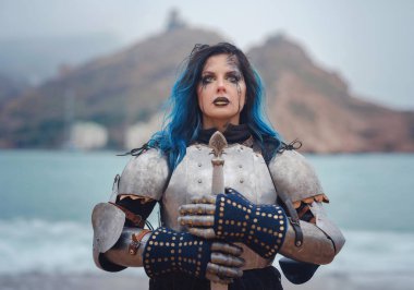 Medieval knight woman in armor prays, blessing before the battle. The Middle Ages history Fantasy photo. Beautiful female knight on the beach near mountains watching snow over sea