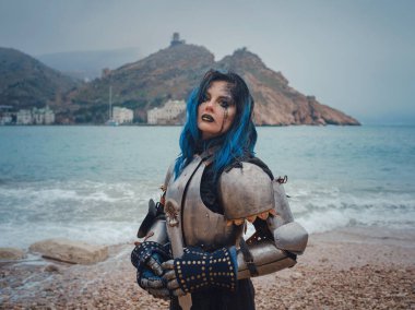 Medieval knight woman in armor prays, blessing before the battle. The Middle Ages history Fantasy photo. Beautiful female knight on the beach near mountains watching snow over sea