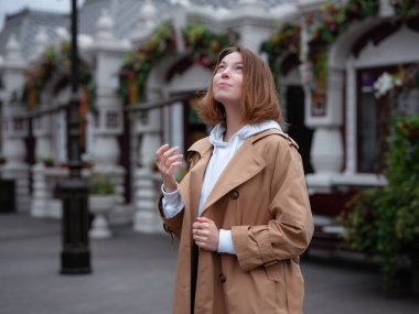 Güzel bej ceketli güzel bir kadın sonbahar bulutlu Moskova 'da yürüyor, sıcak yağmur damlalarından hoşlanıyor. Sokak tarzı. Rusya 'ya Seyahat.